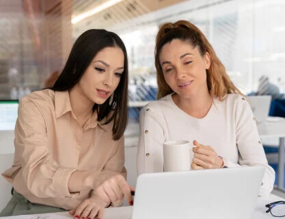 Two female professionals collaborating over a laptop in a modern office, highlighting the technical support and communication skills central to IT and BPO services.